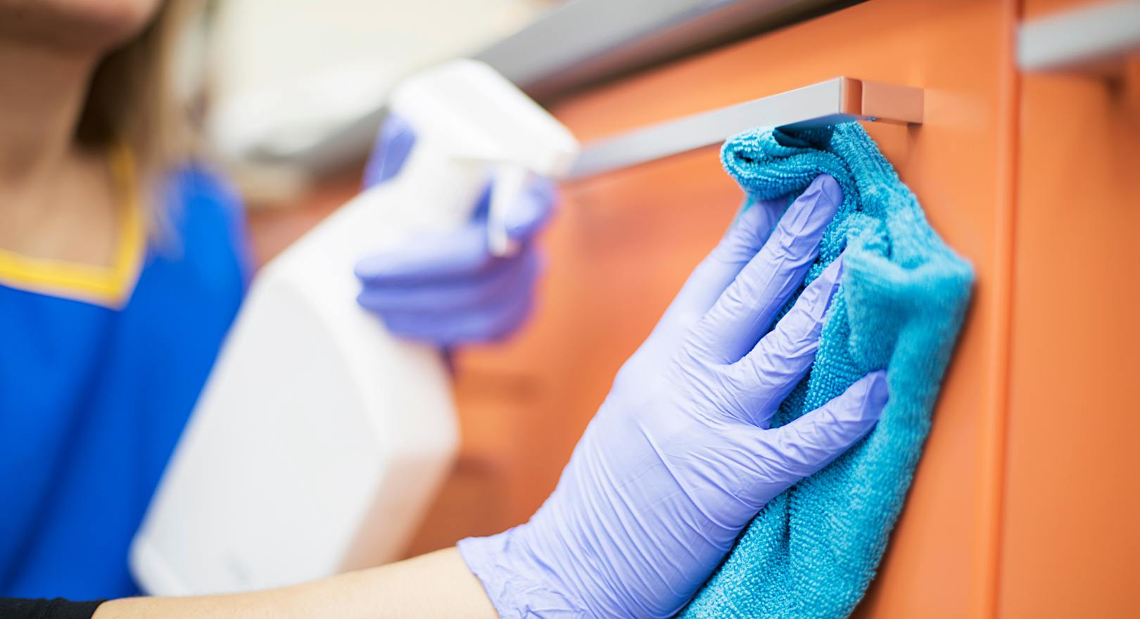 kobieta myje szafkę profesjonalnym środkiem czystości i mikrofibrą