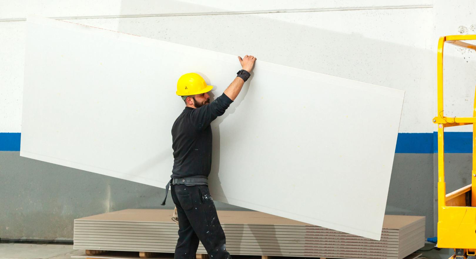 pracownik przenosi płytę z karton-gipsu (GK)